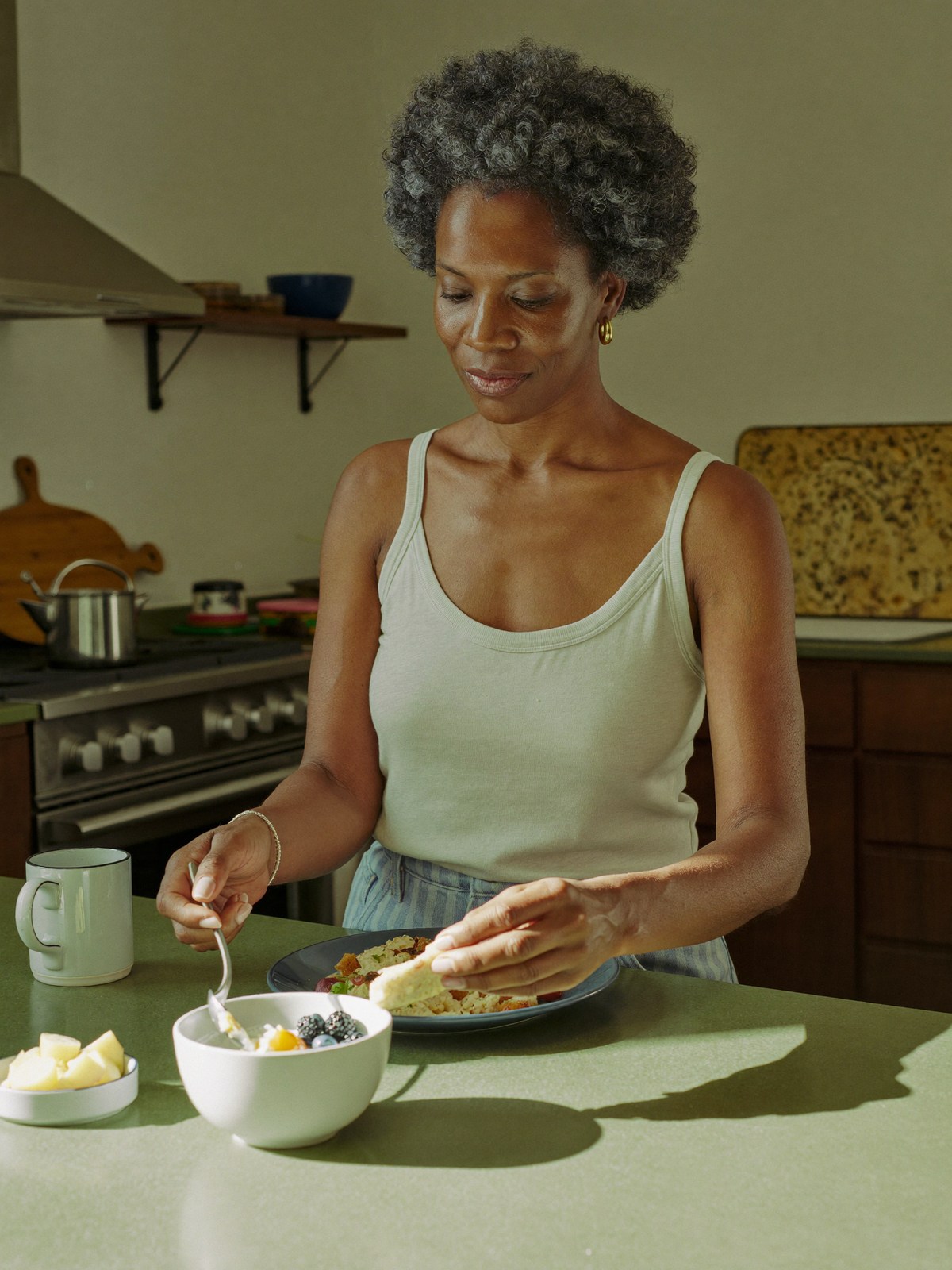 A woman over 40 eating a high-protein breakfast of eggs, yogurt, and berries in a sunlit kitchen